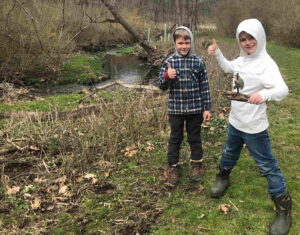 Two boys by a stream with thumbs up
